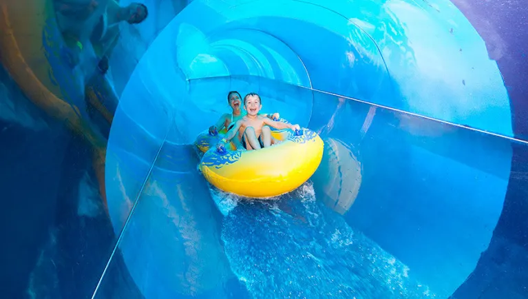 A mother and son smile at the camera as they ride a tube down a water slide at a Great Wolf Lodge indoor water park.